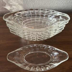 A stack of six clear vintage glass oval dishes with tab handles and a ribbed, thumbprint pattern, ready for ice cream or relishes.