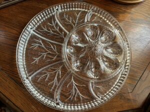 A large, round vintage clear pressed glass serving platter with a central bowl, featuring a 'Tree of Life' or 'Pebble Leaf' design and indentations for deviled eggs.