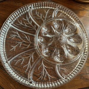 A large, round vintage clear pressed glass serving platter with a central bowl, featuring a 'Tree of Life' or 'Pebble Leaf' design and indentations for deviled eggs.