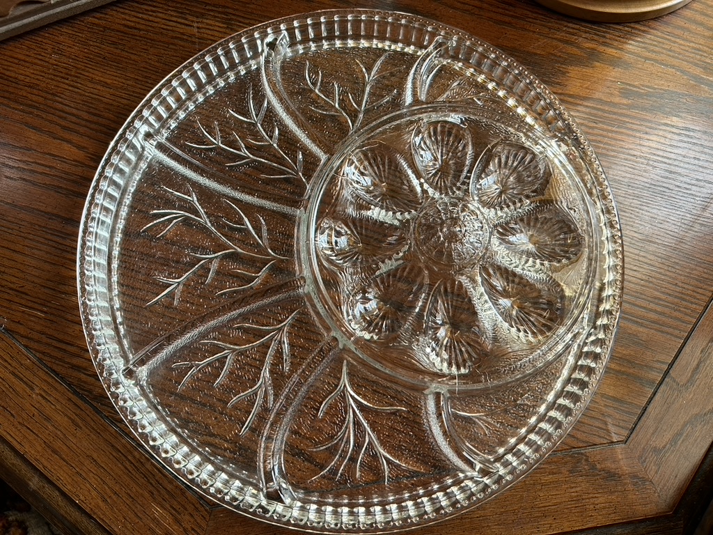 A large, round vintage clear pressed glass serving platter with a central bowl, featuring a 'Tree of Life' or 'Pebble Leaf' design and indentations for deviled eggs.